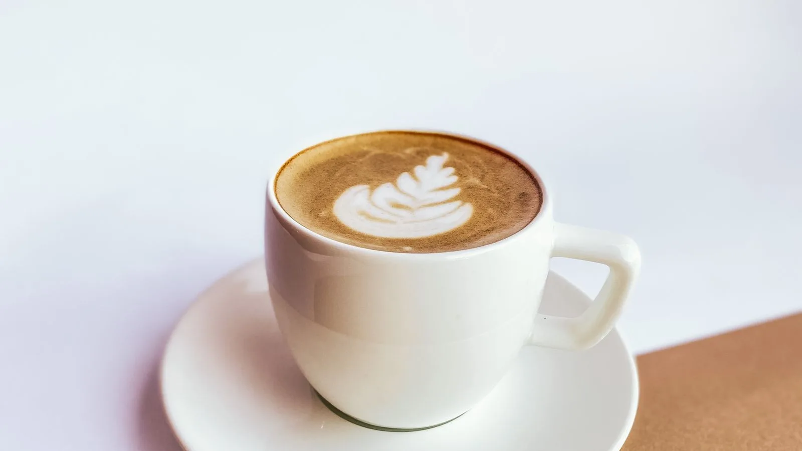 Photo by Olena Ushakova on Pexels A white cup of milk coffee with leaf-shaped foam art on a saucer