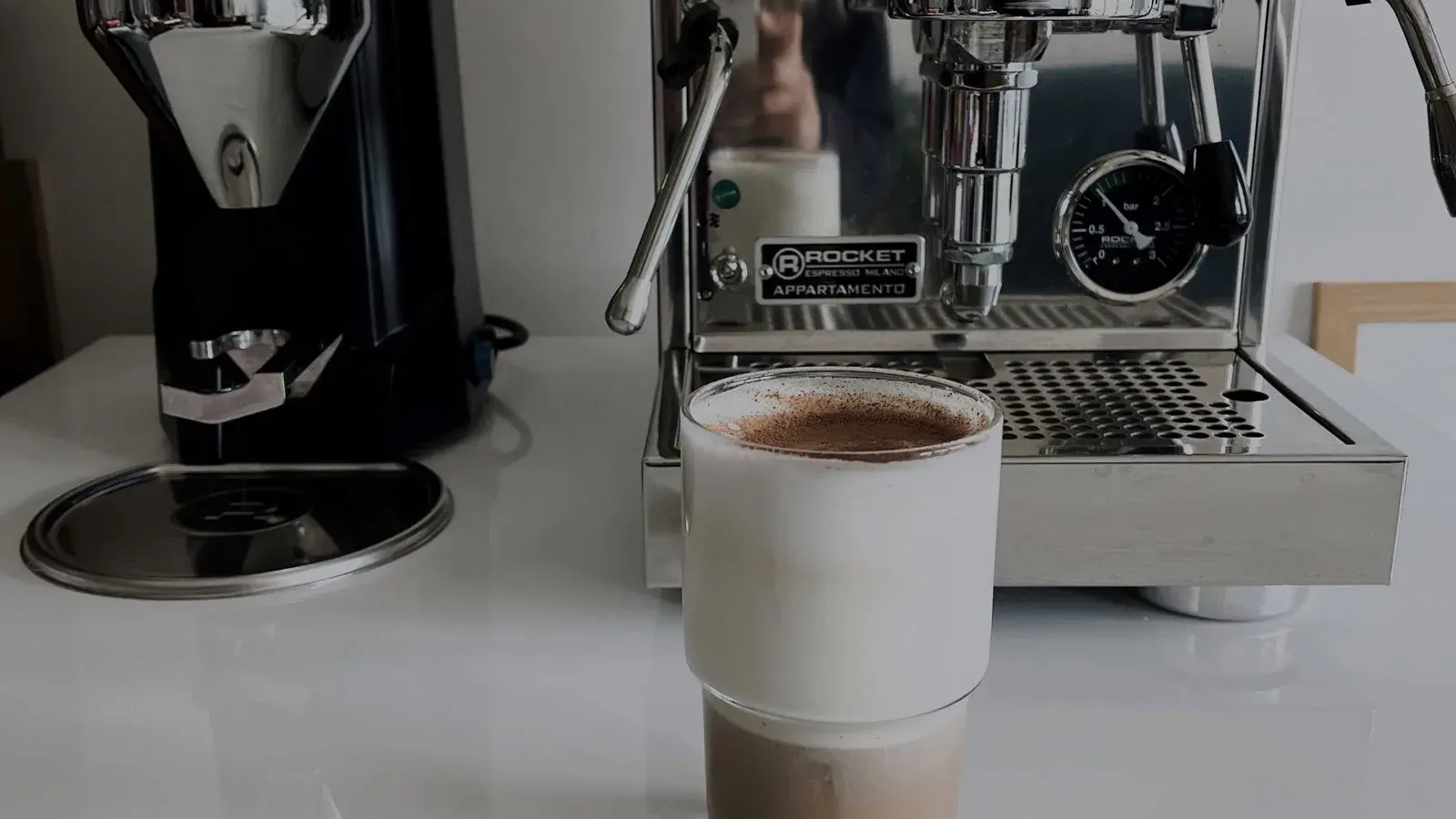 Photo by Feyza Yaşar on Pexels A white cup of coffee in front of a stainless steel espresso machine and grinder