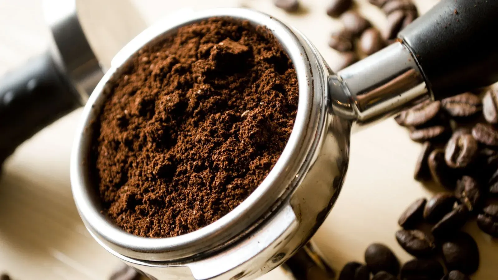 Photo by Pixabay on Pexels Loose coffee grounds in a portafilter basket beside roasted beans