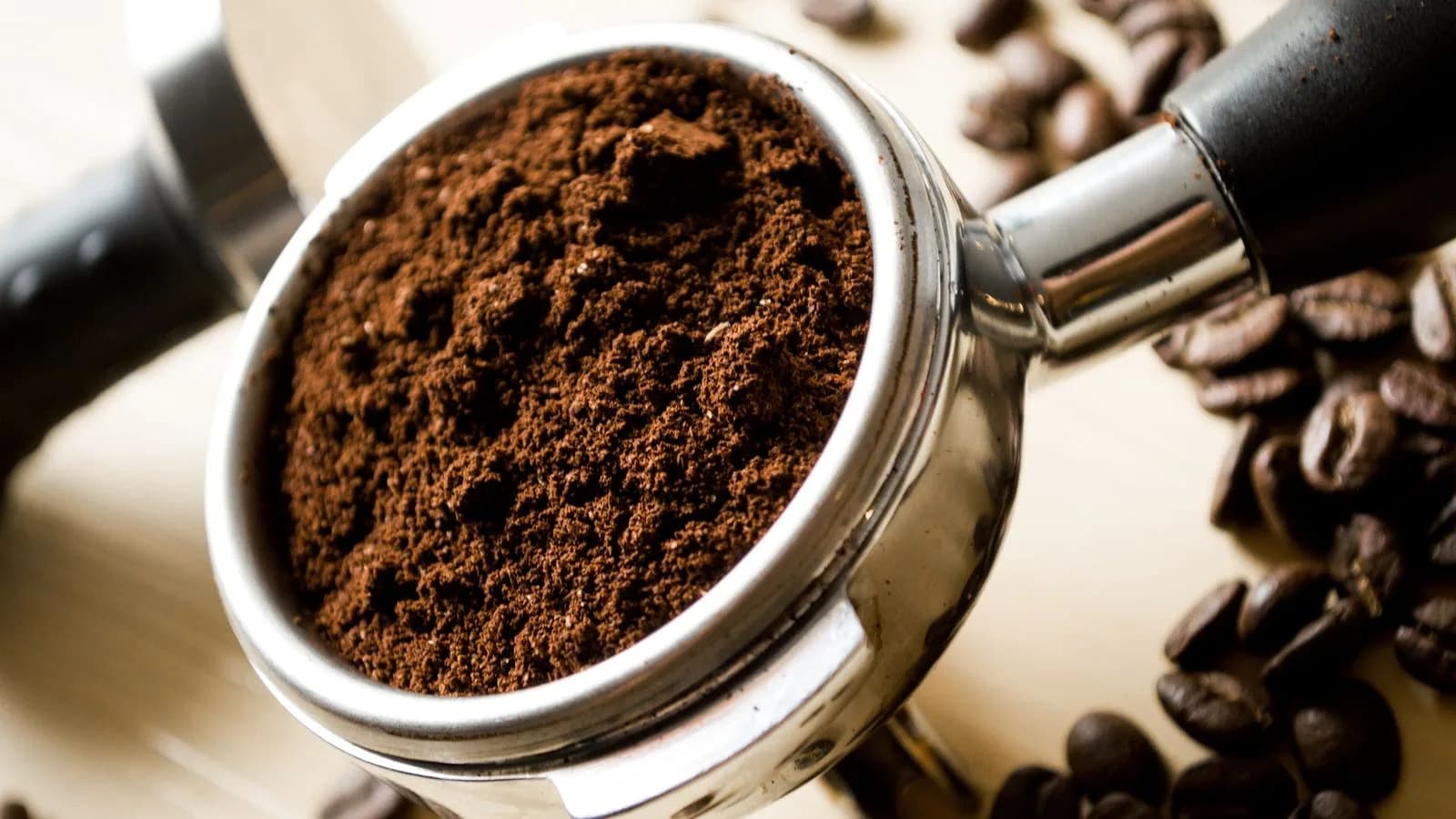 Loose coffee grounds in a portafilter basket beside roasted beans