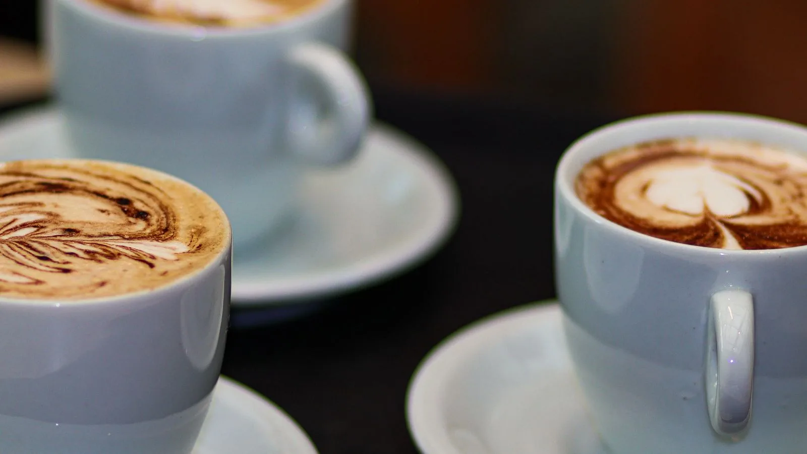 Three milk coffees with latte art in white cups