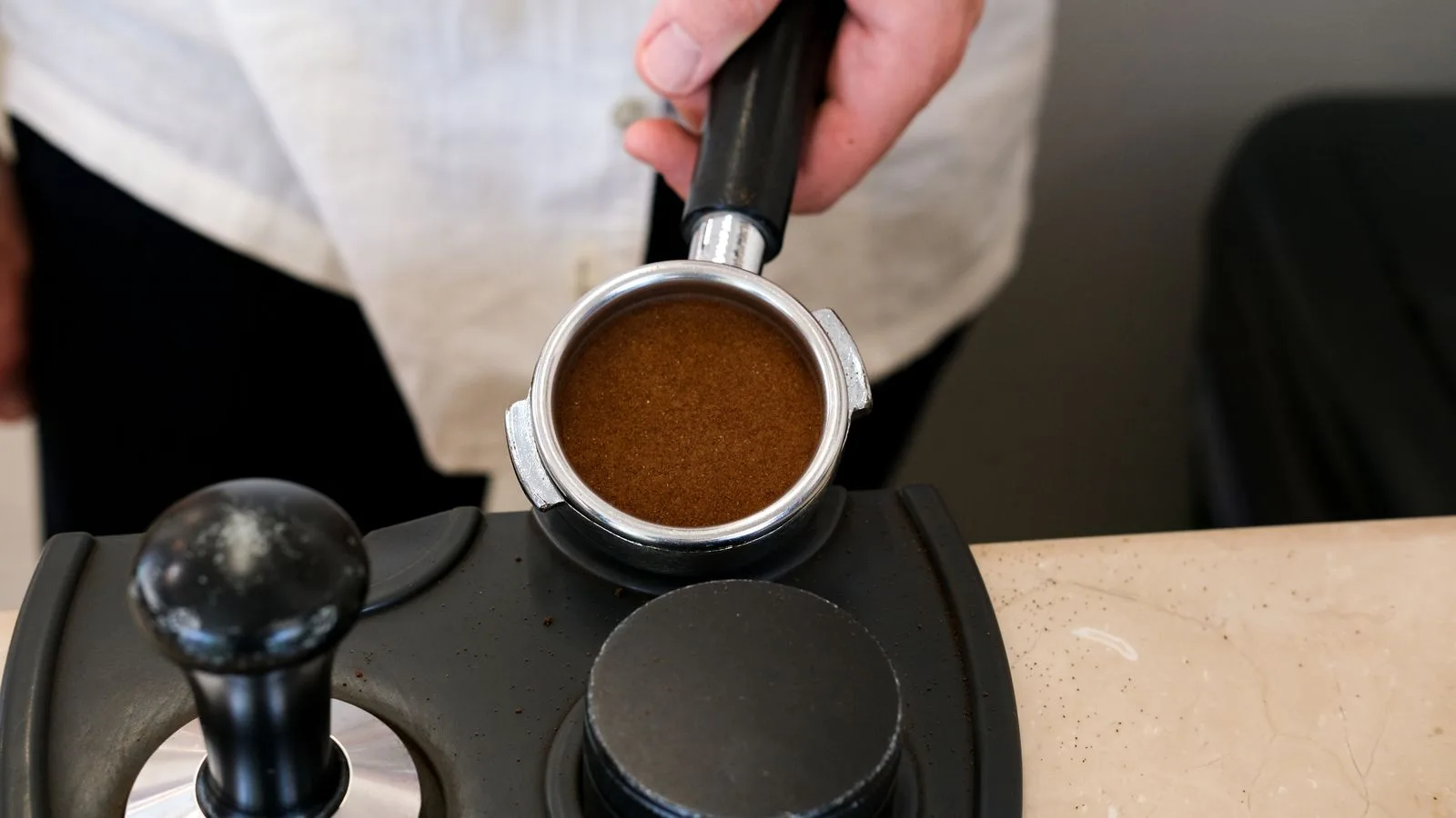 A barista holding a portafilter with tamped coffee grounds