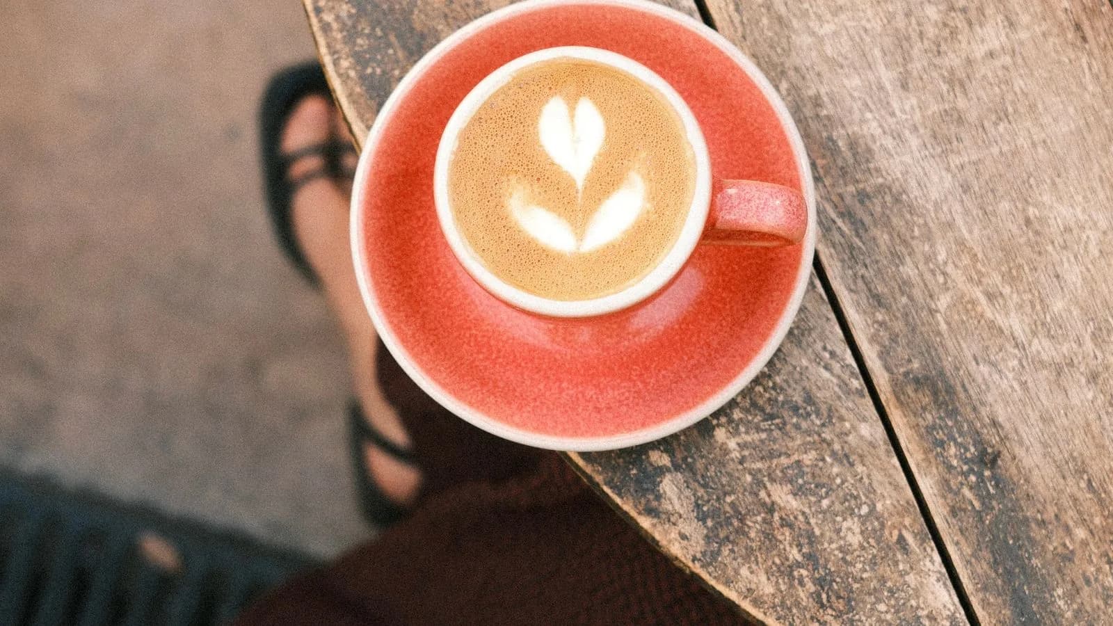 Photo by Chantal Lenting on Pexels A small red cup of coffee with white latte art on a wooden café table