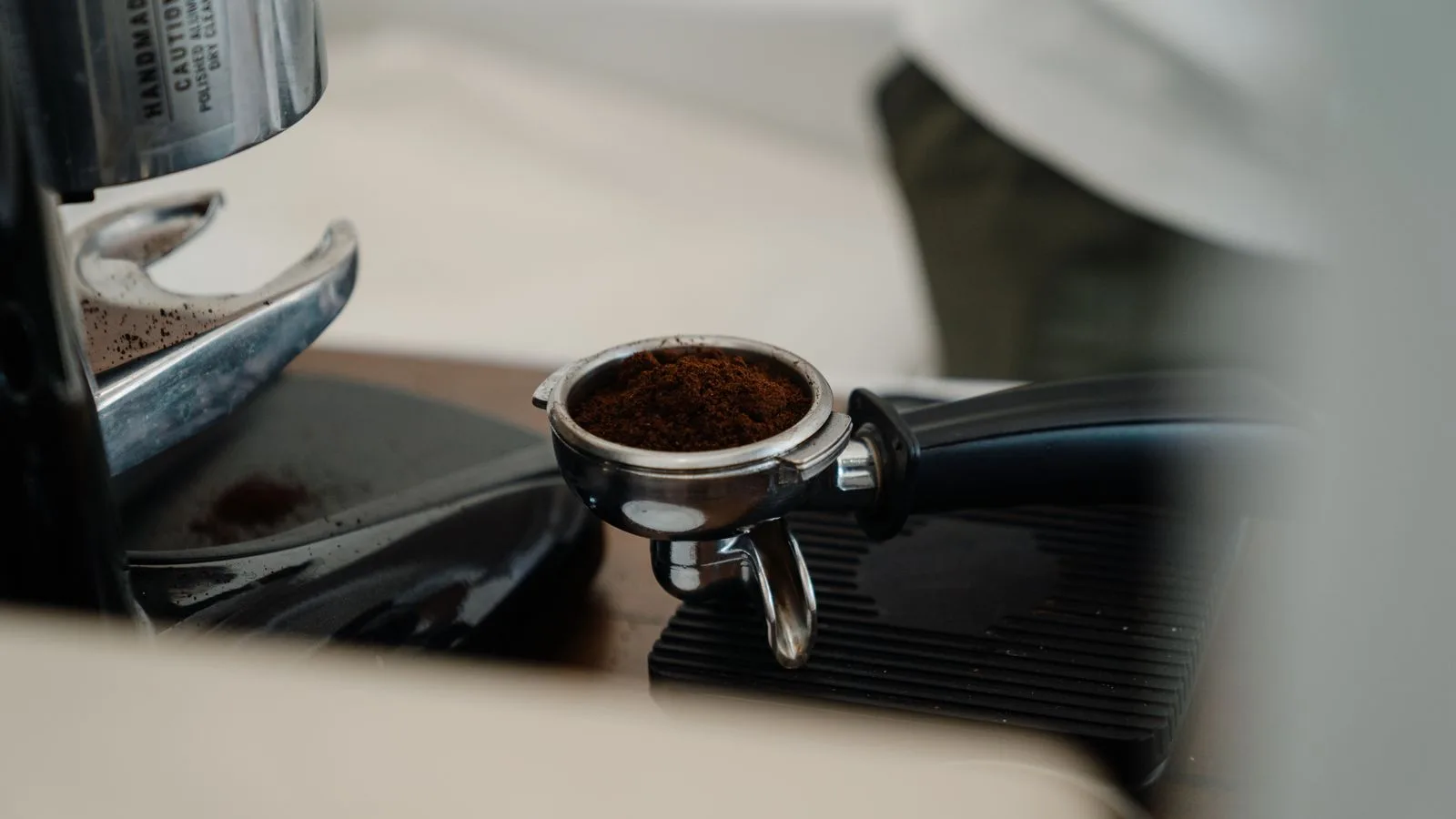 A basket of ground coffee beneath a grinder
