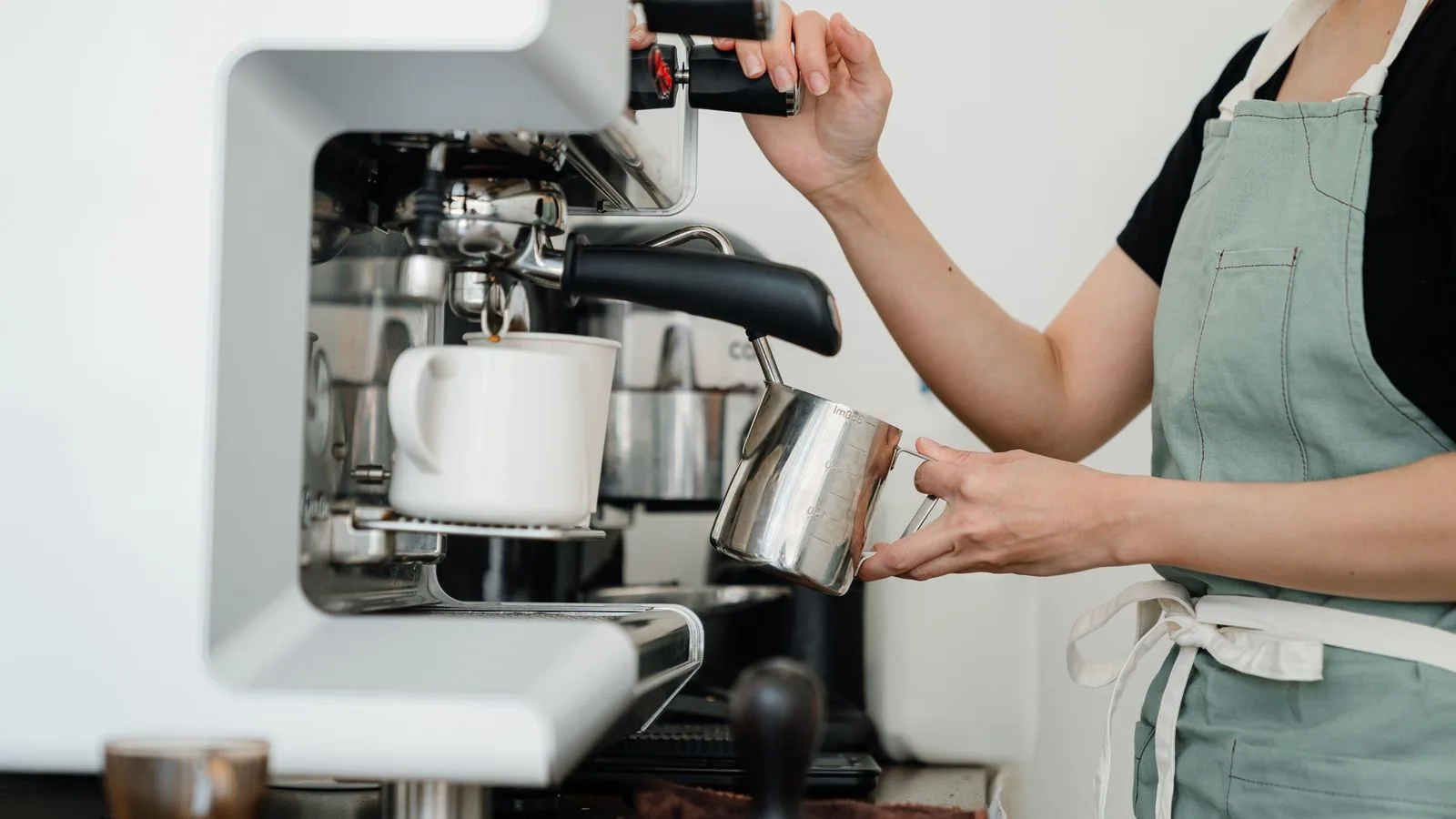 A barista steaming milk beside an espresso machine