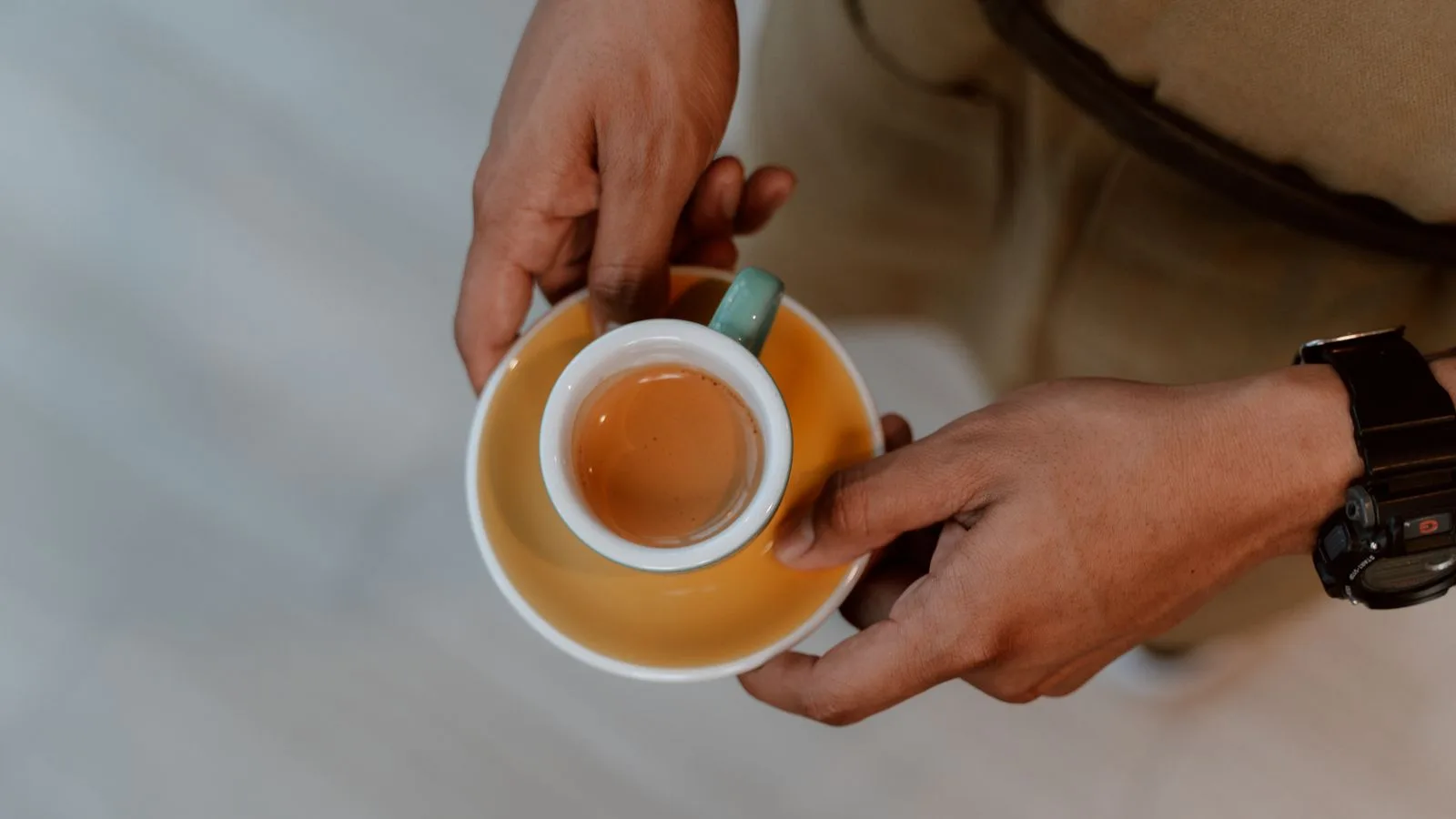 A person holding a cup of espresso on a yellow saucer