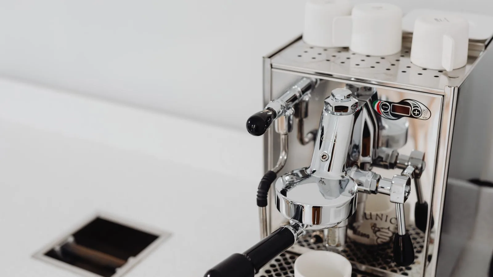 An espresso machine with cups on top beside a sink