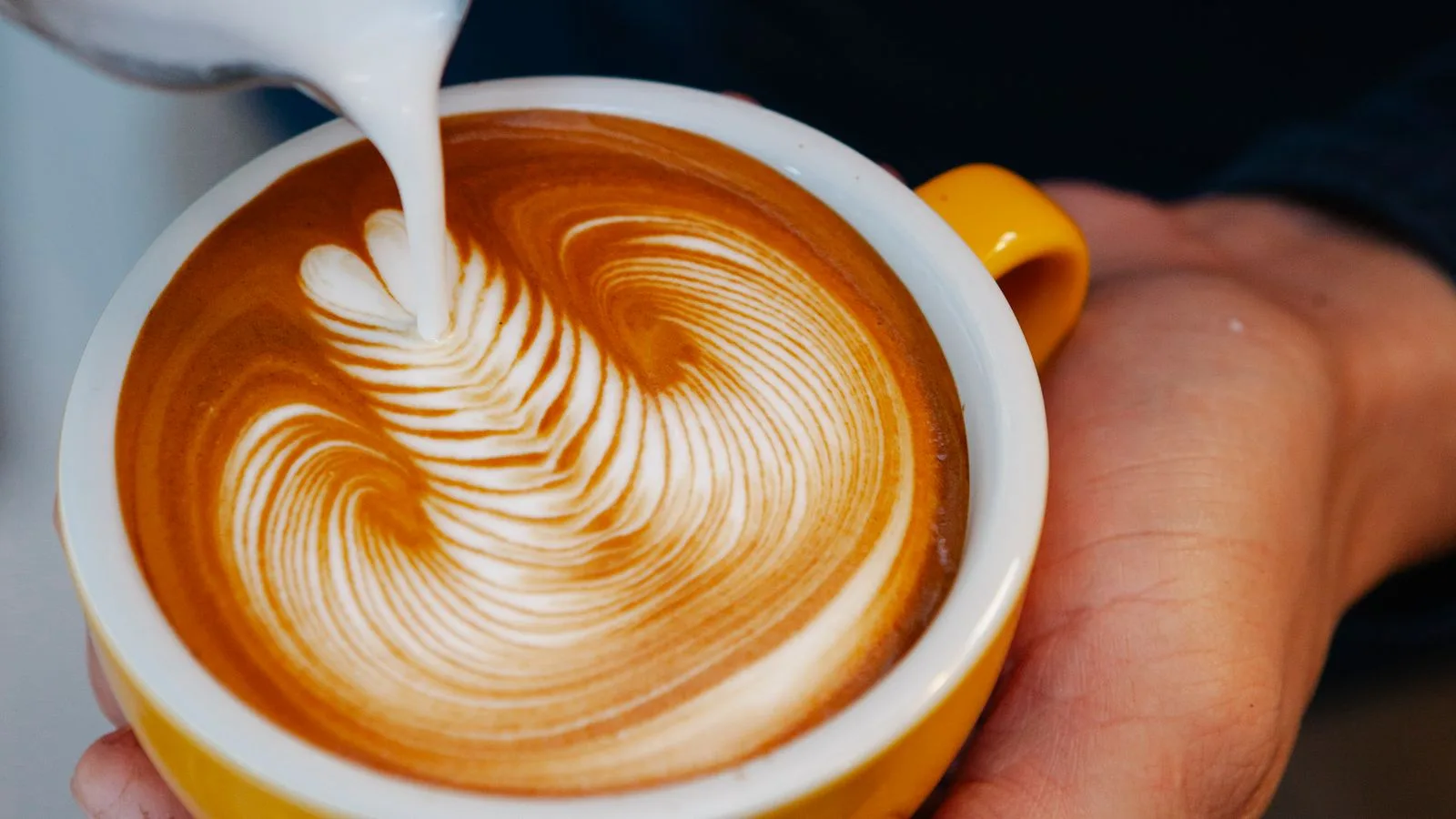 Milk poured into a yellow cup to form latte art