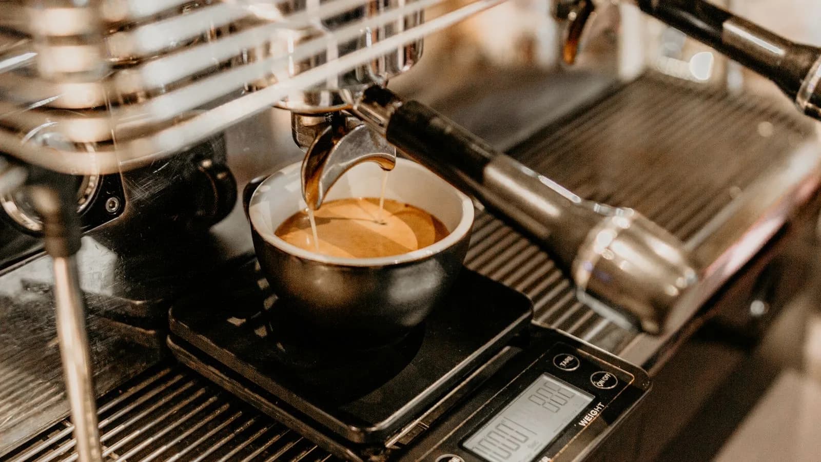 Photo by Marta Dzedyshko on Pexels Espresso pouring from a portafilter into a cup that sits on a black digital scale on an espresso machine drip tray